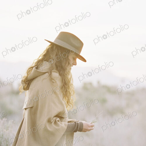 A woman in a warm coat and a hat picking wild flowers.