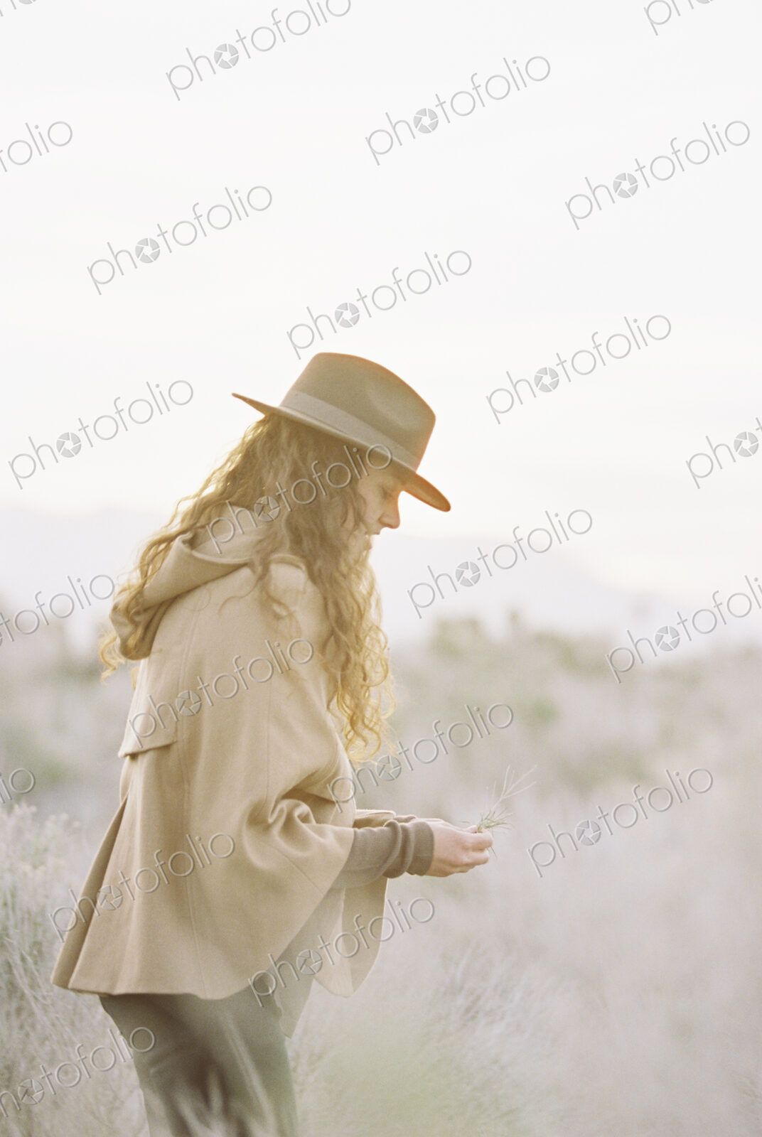 A woman in a warm coat and a hat picking wild flowers.