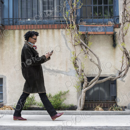 A woman in a warm coat walking along the street, checking her phone.