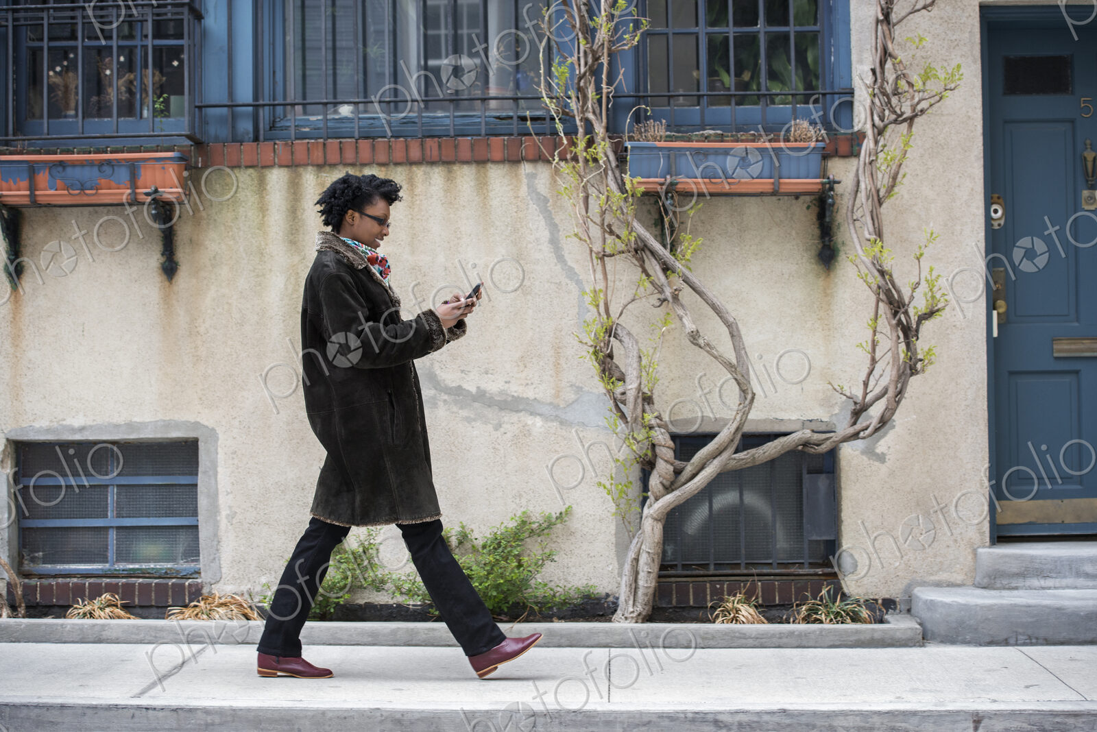 A woman in a warm coat walking along the street, checking her phone.