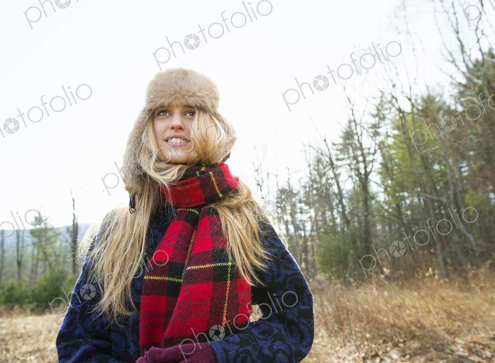A woman in a warm furry hat and a big red tartan scarf, outdoors in the winter.