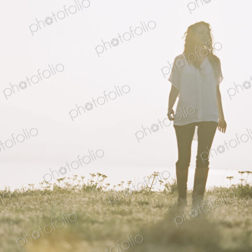 A woman in a white shirt with long hair standing outdoors looking around her.