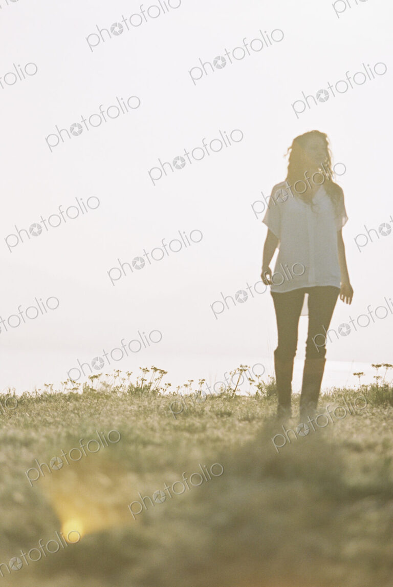 A woman in a white shirt with long hair standing outdoors looking around her.