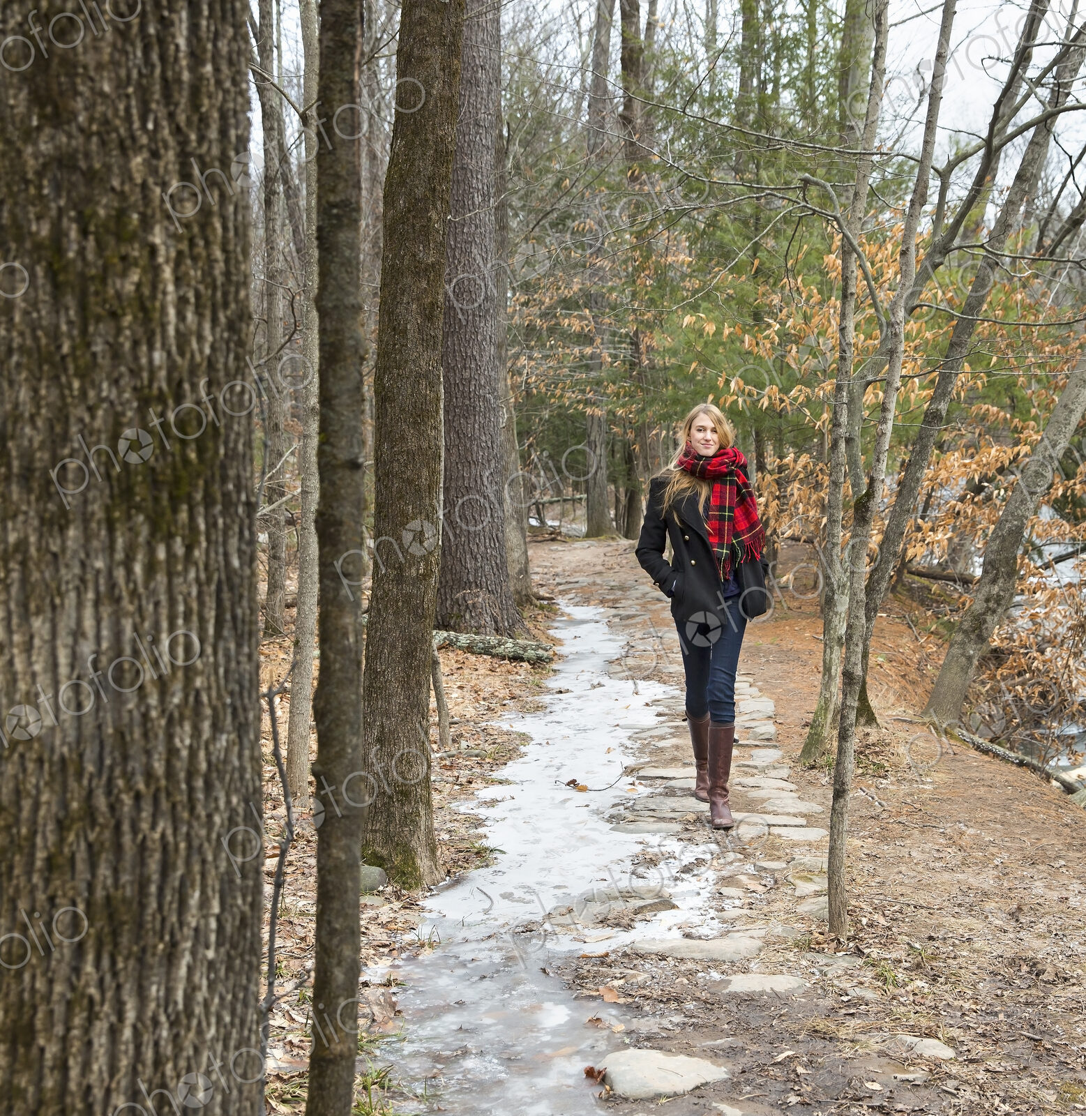 A woman in a winter coat and red scarf walking down a woodland path, in winter.