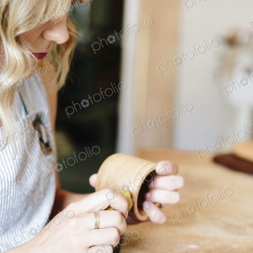 A woman in a workshop using a slab of wax to oil a small wood turned cup or bowl.