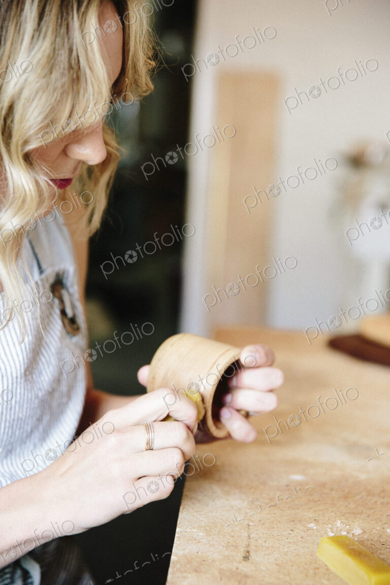 A woman in a workshop using a slab of wax to oil a small wood turned cup or bowl.