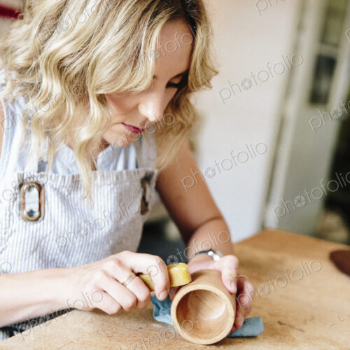A woman in a workshop using a slab of wax to oil a small wood turned cup or bowl.