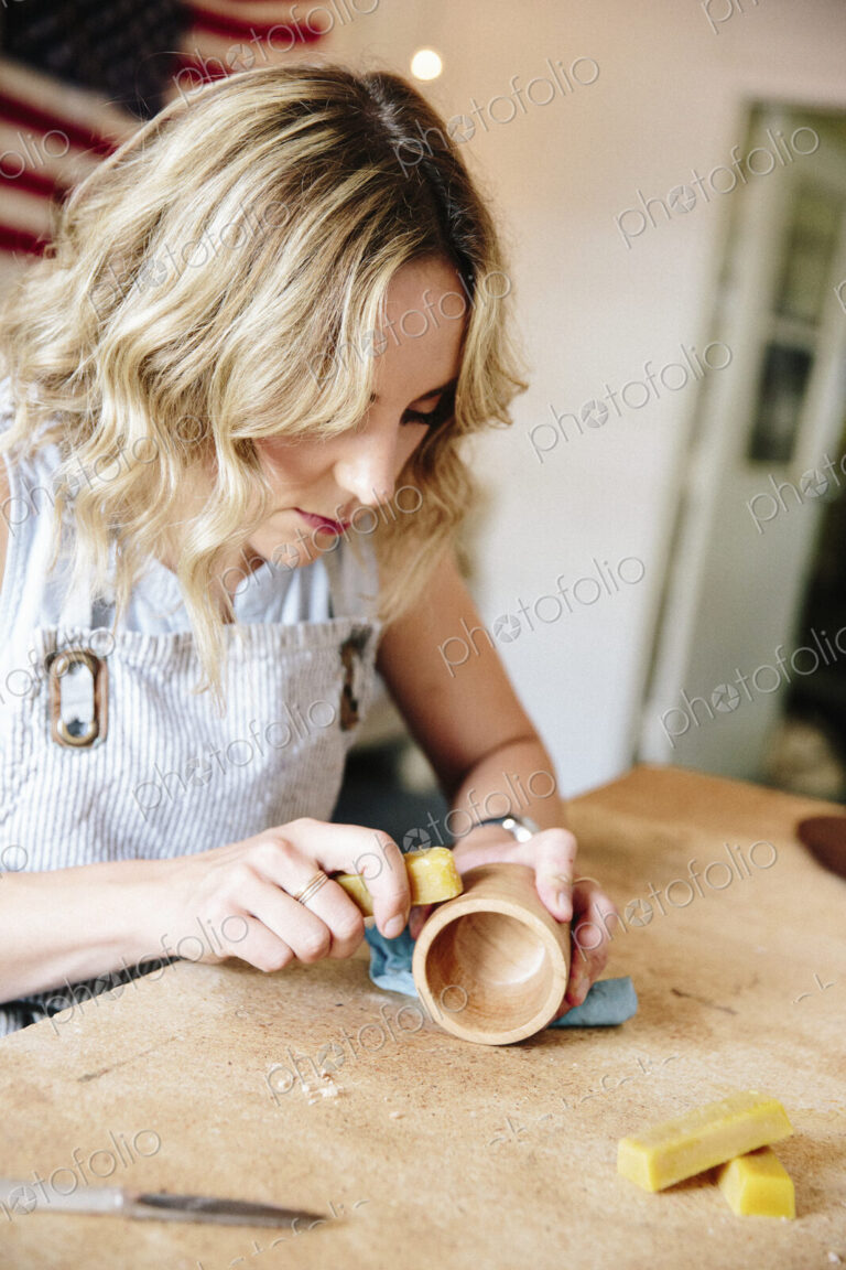 A woman in a workshop using a slab of wax to oil a small wood turned cup or bowl.