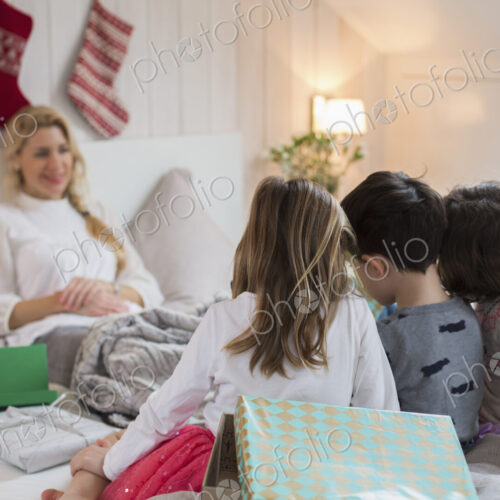 A woman in bed, with three children at the foot of the bed, carrying Christmas presents. A woman in bed, with three children at the foot of the bed, carrying Christmas presents.