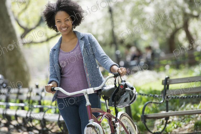 A woman in casual clothes in the park pushing a bicycle.