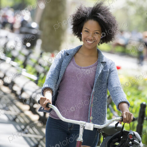 A woman in casual clothes in the park pushing a bicycle.
