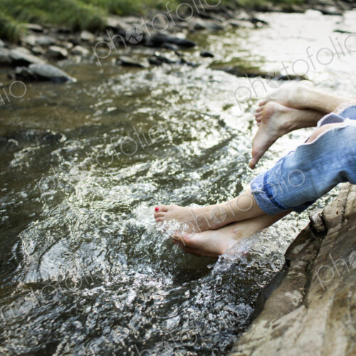 A woman in fashionable jeans with a rip, with her feet in the cool flowing waters of a… A woman in fashionable jeans with a rip, with her feet in the cool flowing waters of a…