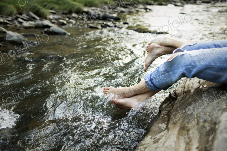 A woman in fashionable jeans with a rip, with her feet in the cool flowing waters of a…