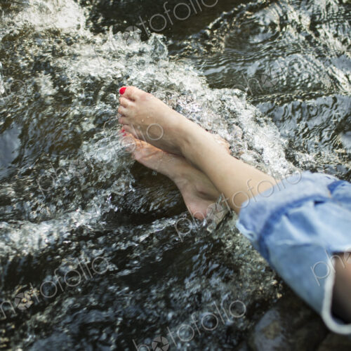 A woman in fashionable jeans with a rip, with her feet in the cool flowing waters of a…