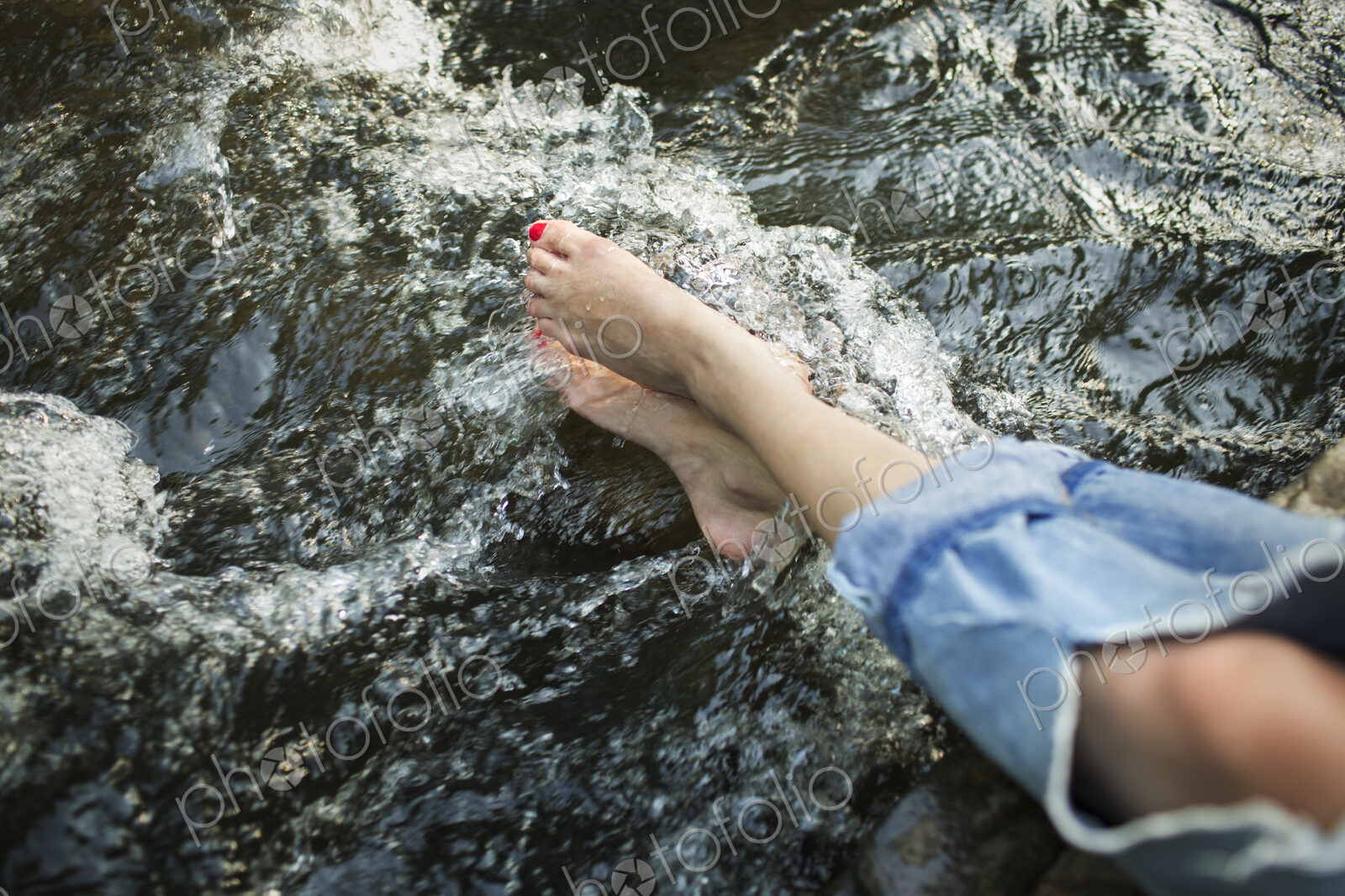 A woman in fashionable jeans with a rip, with her feet in the cool flowing waters of a…
