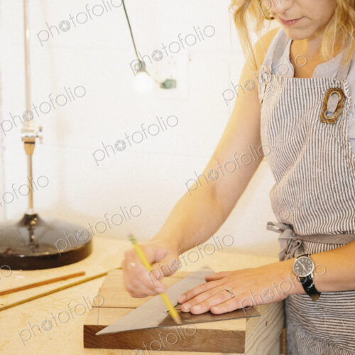 A woman in her workshop using a template to mark wooden blocks.