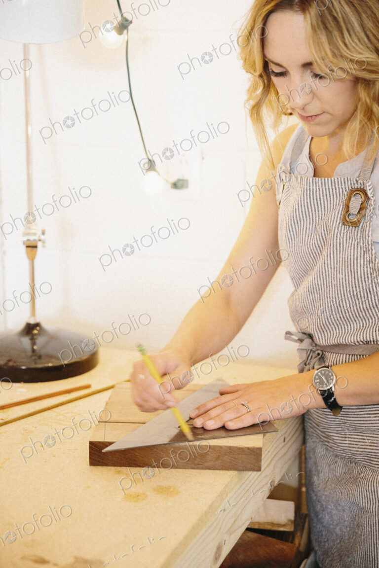 A woman in her workshop using a template to mark wooden blocks.