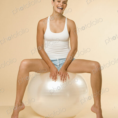 A woman in vest and shorts sitting on an exercise ball.