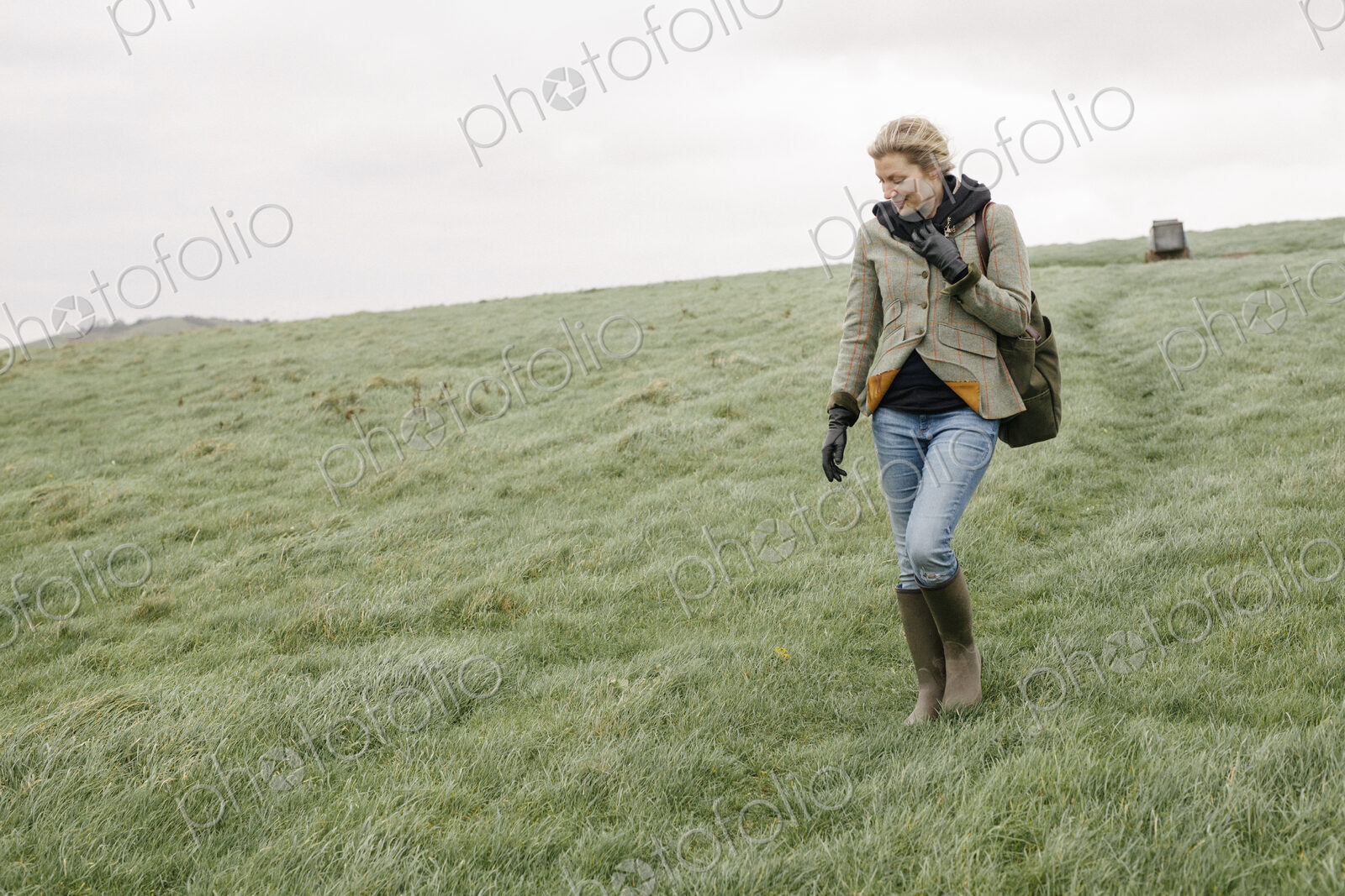 A woman in warm coat and gloves walking across open country, grassland and moors.