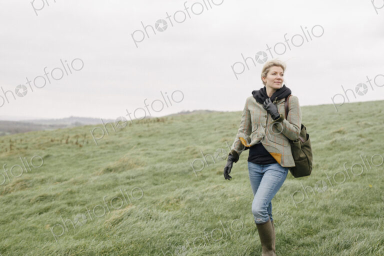 A woman in warm coat and gloves walking across open country, grassland and moors.