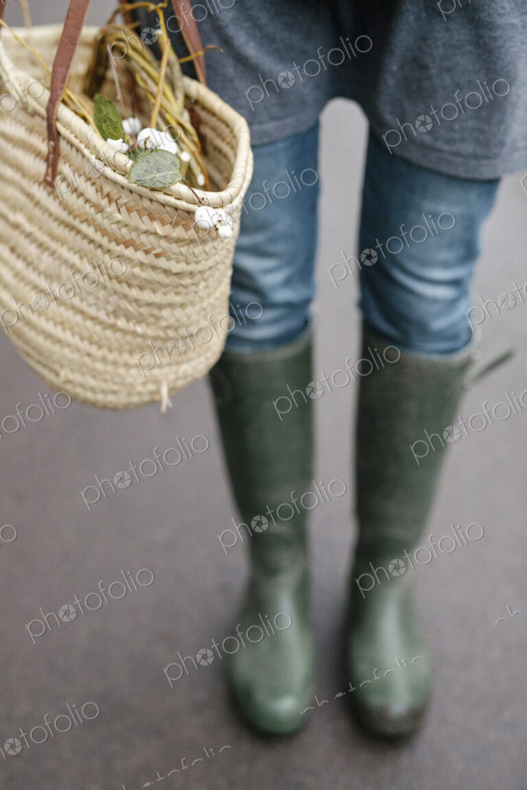 A woman in wellingtons and jeans carrying a basket.