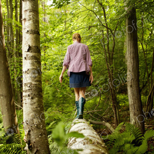 A woman in wellingtons walking along a fallen tree trunk, in woodland. A woman in wellingtons walking along a fallen tree trunk, in woodland.