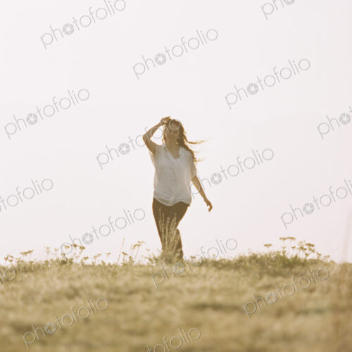 A woman in white shirt and jeans walking across grass.