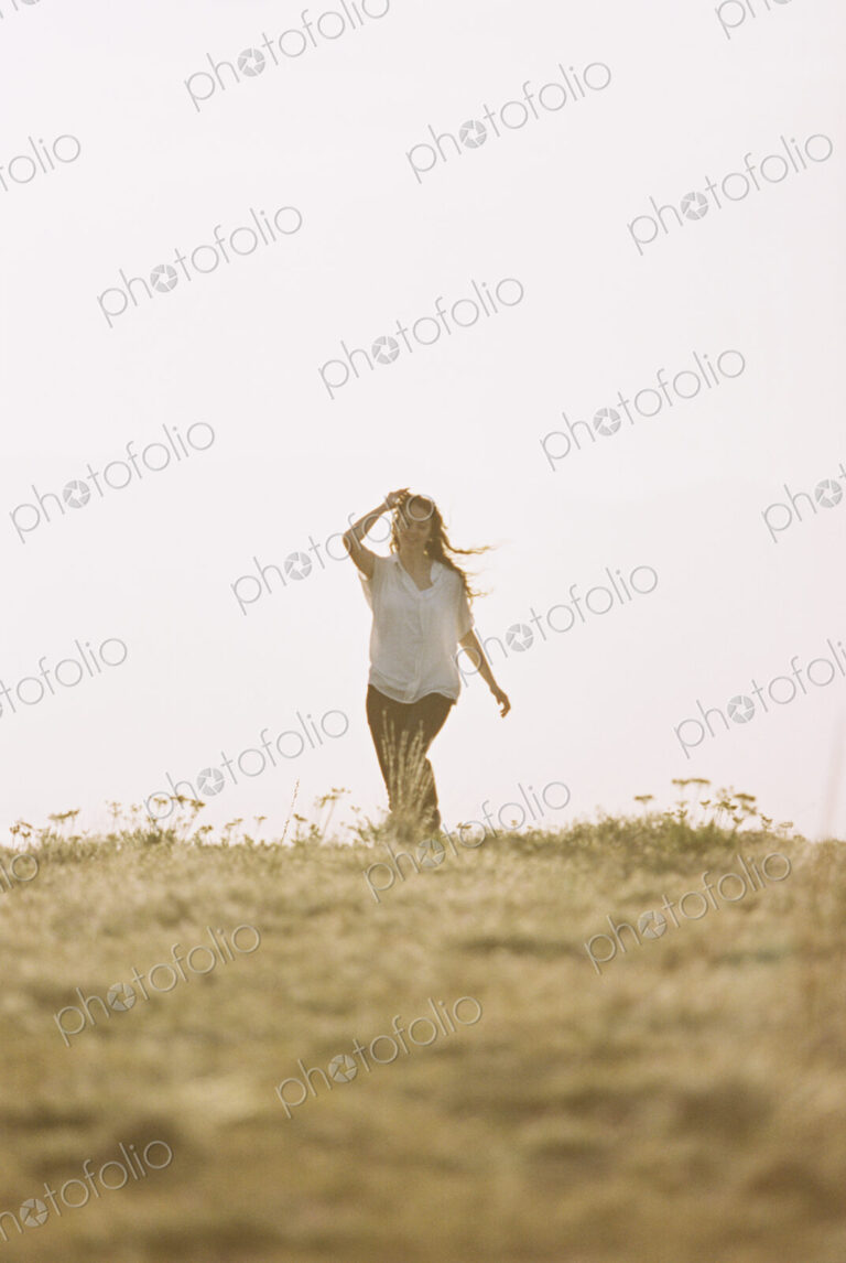 A woman in white shirt and jeans walking across grass.
