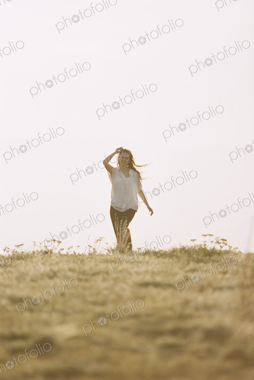 A woman in white shirt and jeans walking across grass.