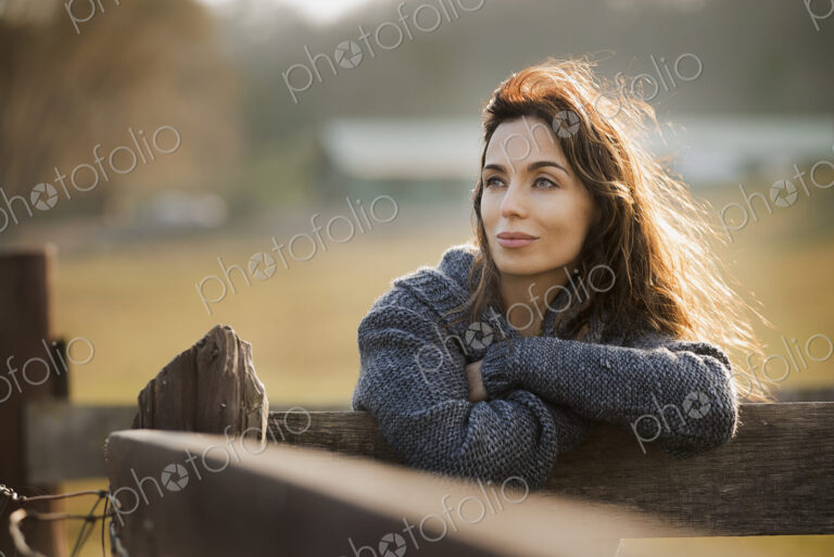 A woman leaning on a fence on an organic farm.