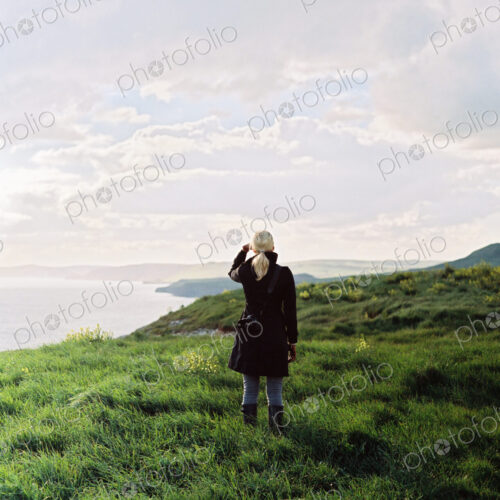A woman looking along the coastline, inlets and cliffs.