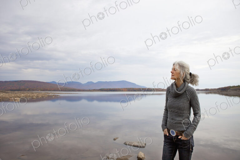 A woman looking out over the water on the shores of a calm lake.