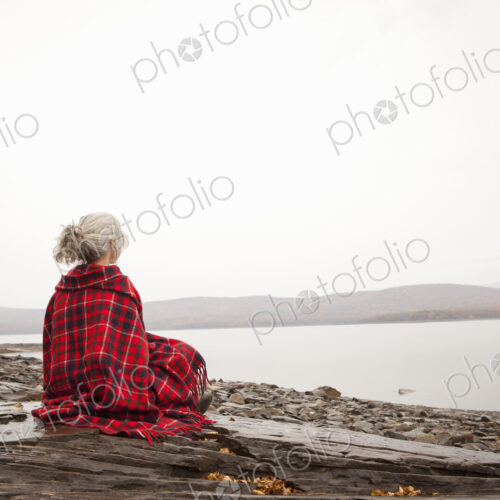 A woman looking out over the water on the shores of a calm lake, wrapped in a tartan rug. A woman looking out over the water on the shores of a calm lake, wrapped in a tartan rug.