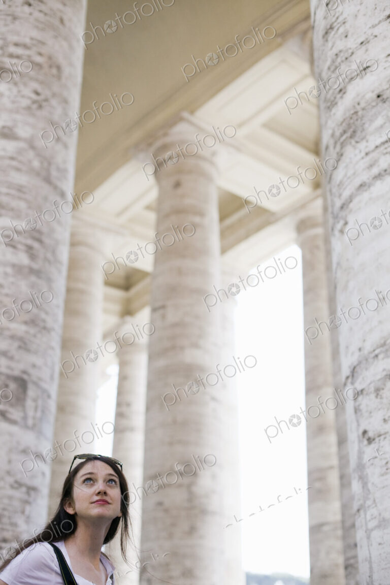 A woman looking up at the tall pillars and arches of a historic building in Rome.