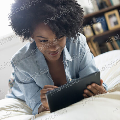 A woman lying on a bed, using a digital tablet. A woman lying on a bed, using a digital tablet.