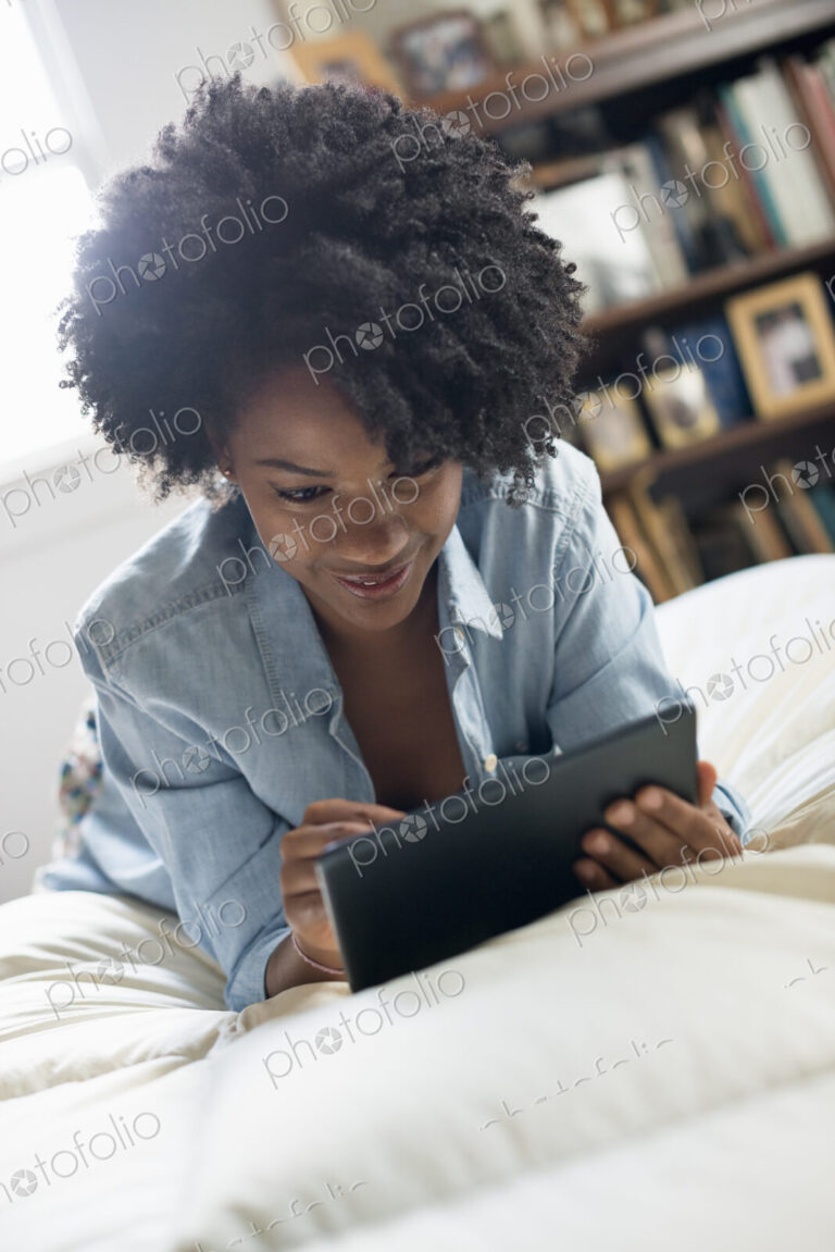 A woman lying on a bed, using a digital tablet.