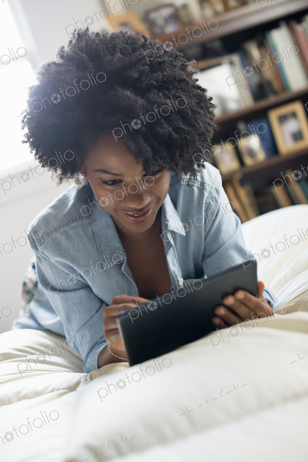 A woman lying on a bed, using a digital tablet.