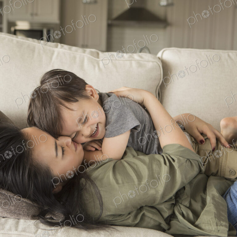 A woman lying on a sofa, smiling, cuddling her young son.
