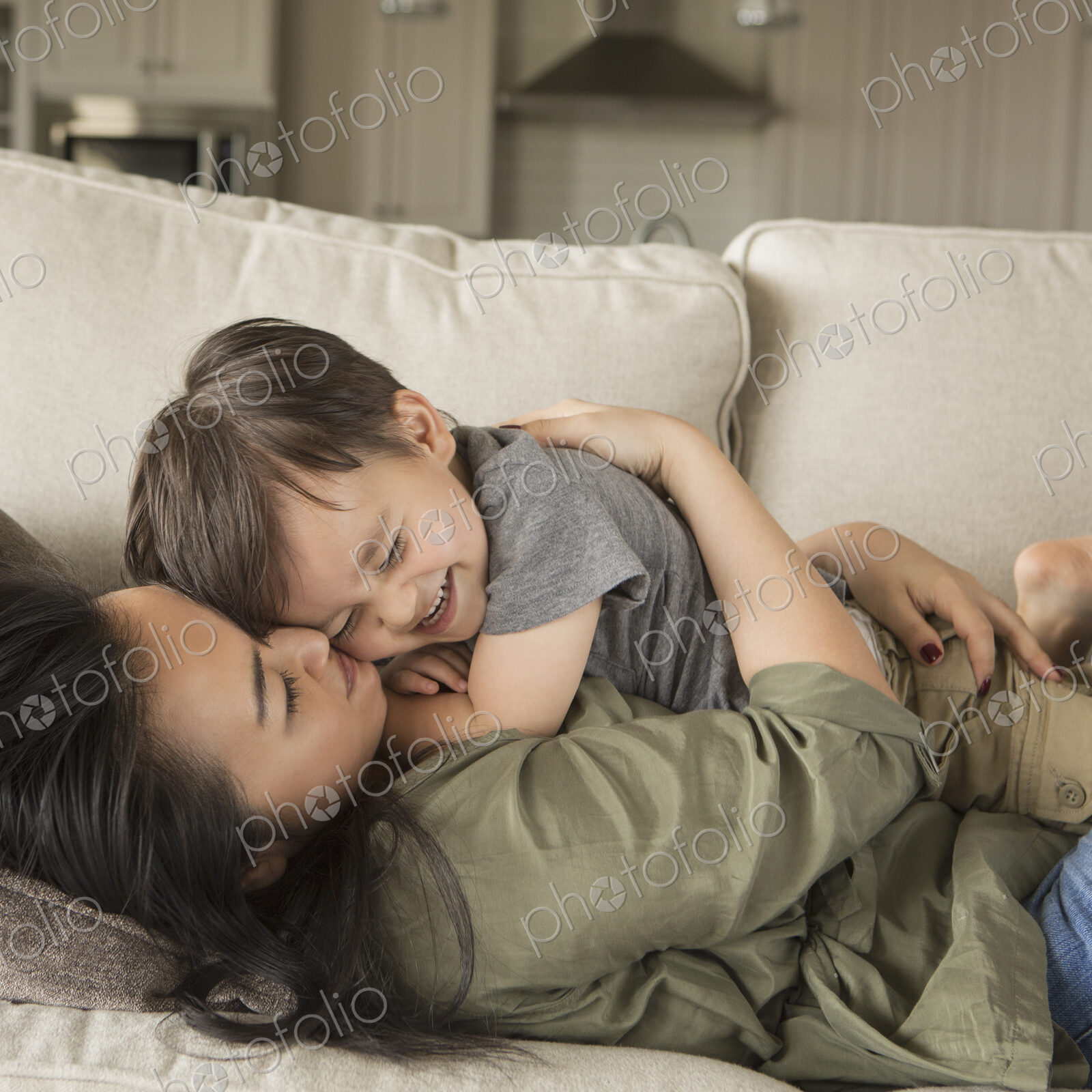 A woman lying on a sofa, smiling, cuddling her young son.