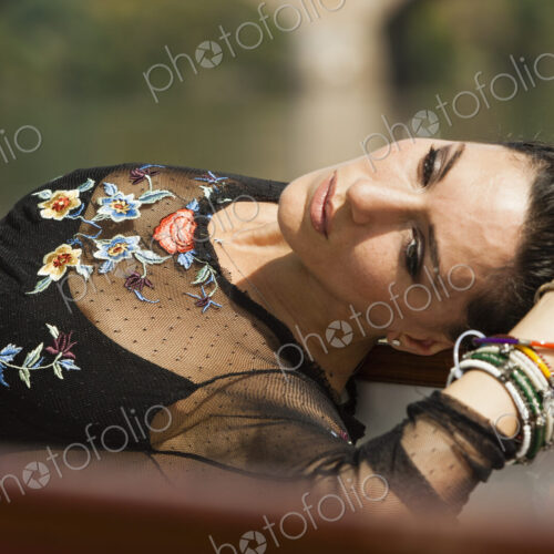 A woman lying on her back with her arm above her head. Wearing a fashionable black top…