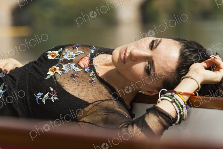 A woman lying on her back with her arm above her head. Wearing a fashionable black top…
