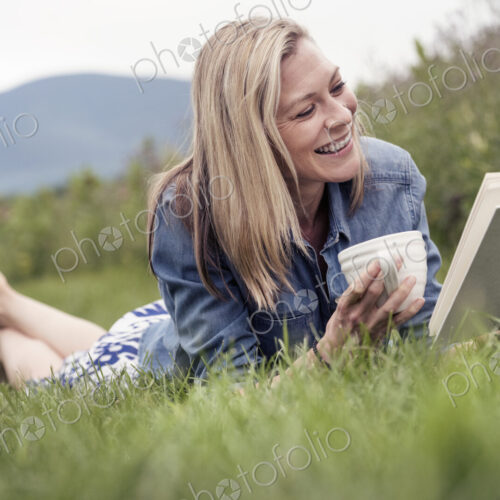 A woman lying on the grass holding a tea cup and reading a book. A woman lying on the grass holding a tea cup and reading a book.