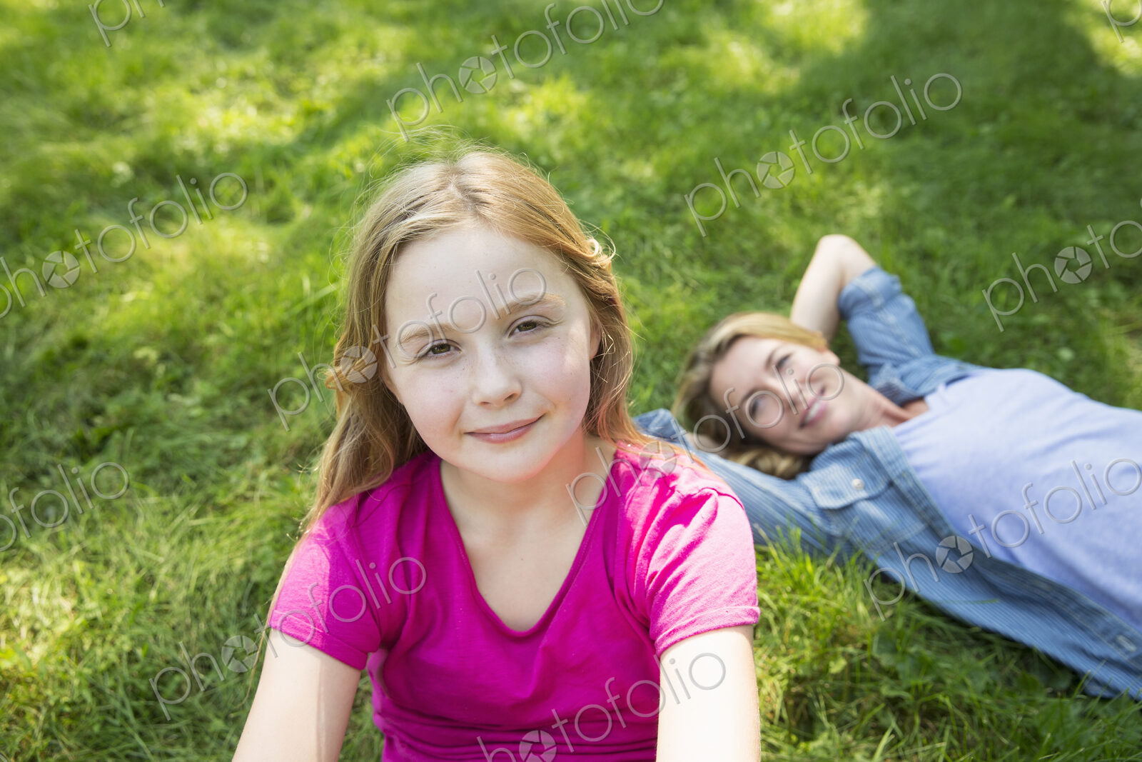 A woman lying on the grass relaxing and a young girl looking at the camera.