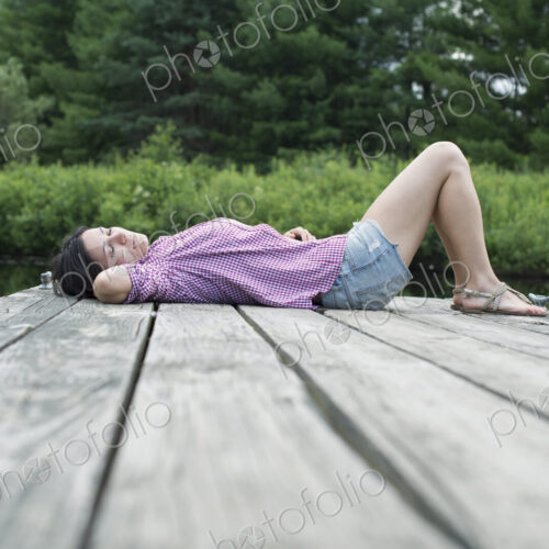 A woman lying on the jetty by a lake in summer