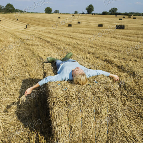 A woman lying on top of a square bale of packed straw at harvest time. A woman lying on top of a square bale of packed straw at harvest time.