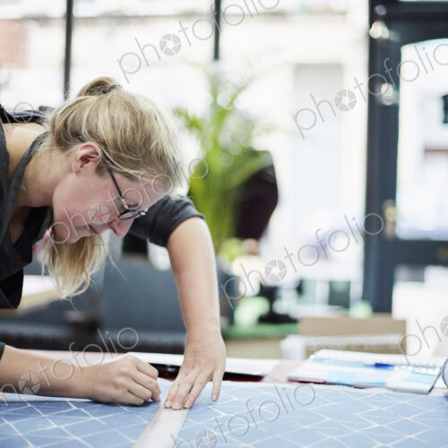 A woman measuring and marking the fabric for an upholstery task in a workshop. A woman measuring and marking the fabric for an upholstery task in a workshop.