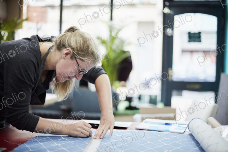 A woman measuring and marking the fabric for an upholstery task in a workshop.