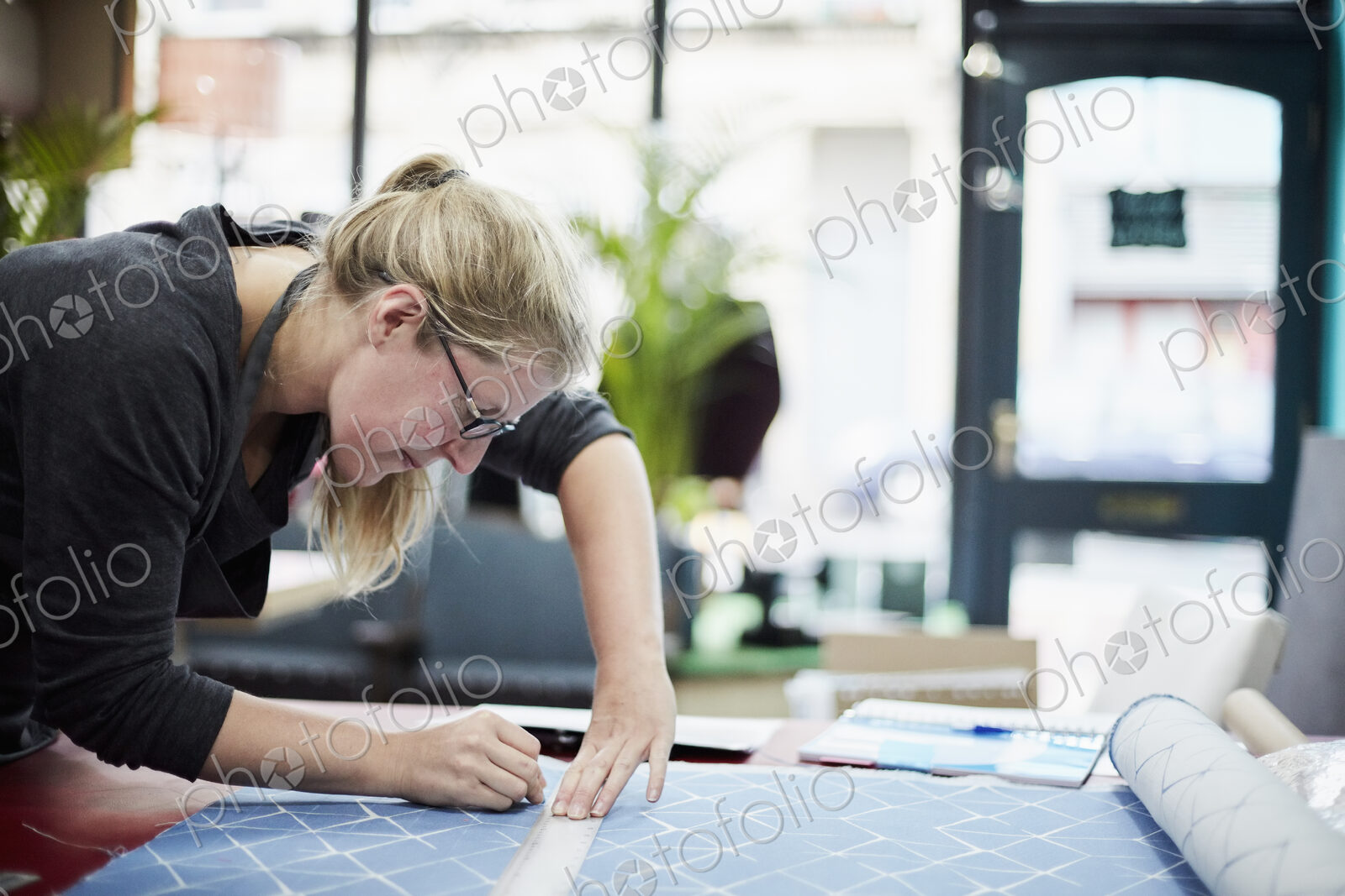 A woman measuring and marking the fabric for an upholstery task in a workshop.