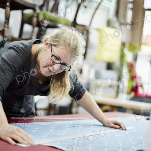 A woman measuring and marking the fabric for an upholstery task in a workshop. A woman measuring and marking the fabric for an upholstery task in a workshop.