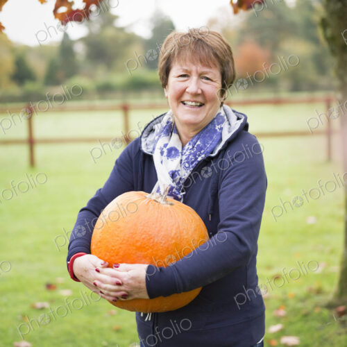 A woman outdoors holding a large orange pumpkin.